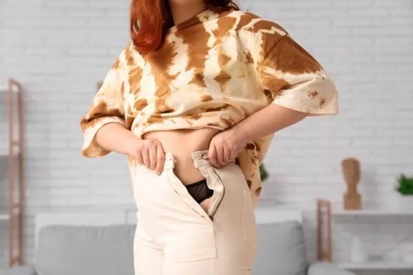 Image of woman trying to do her trousers up after pregnancy weight gain Leigh on Sea